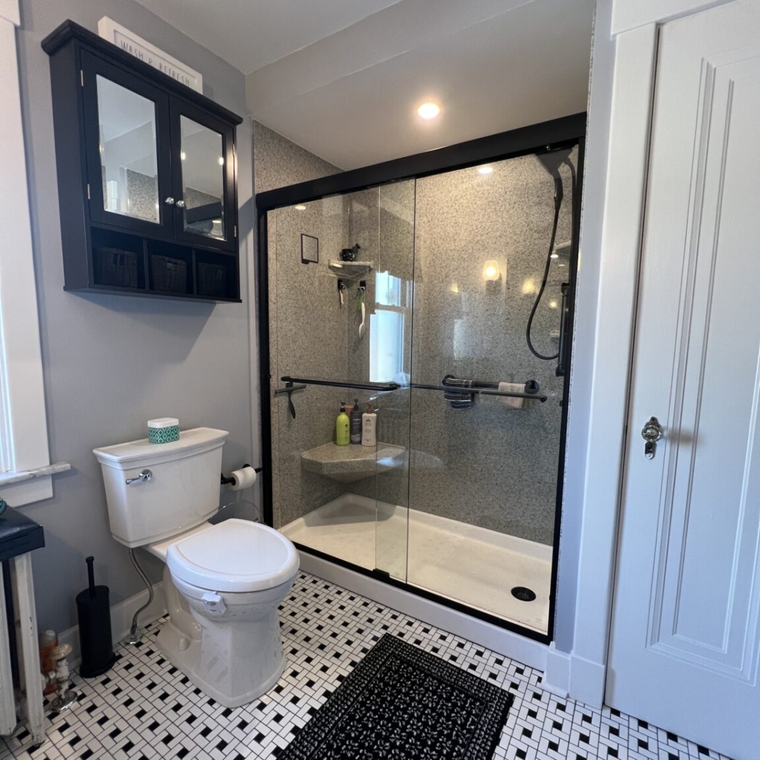 Contemporary small bathroom remodel with black frame, tub to shower conversion, black and white floor tile, two-piece toilet