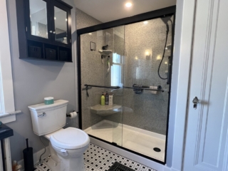 Contemporary small bathroom remodel with black frame, tub to shower conversion, black and white floor tile, two-piece toilet