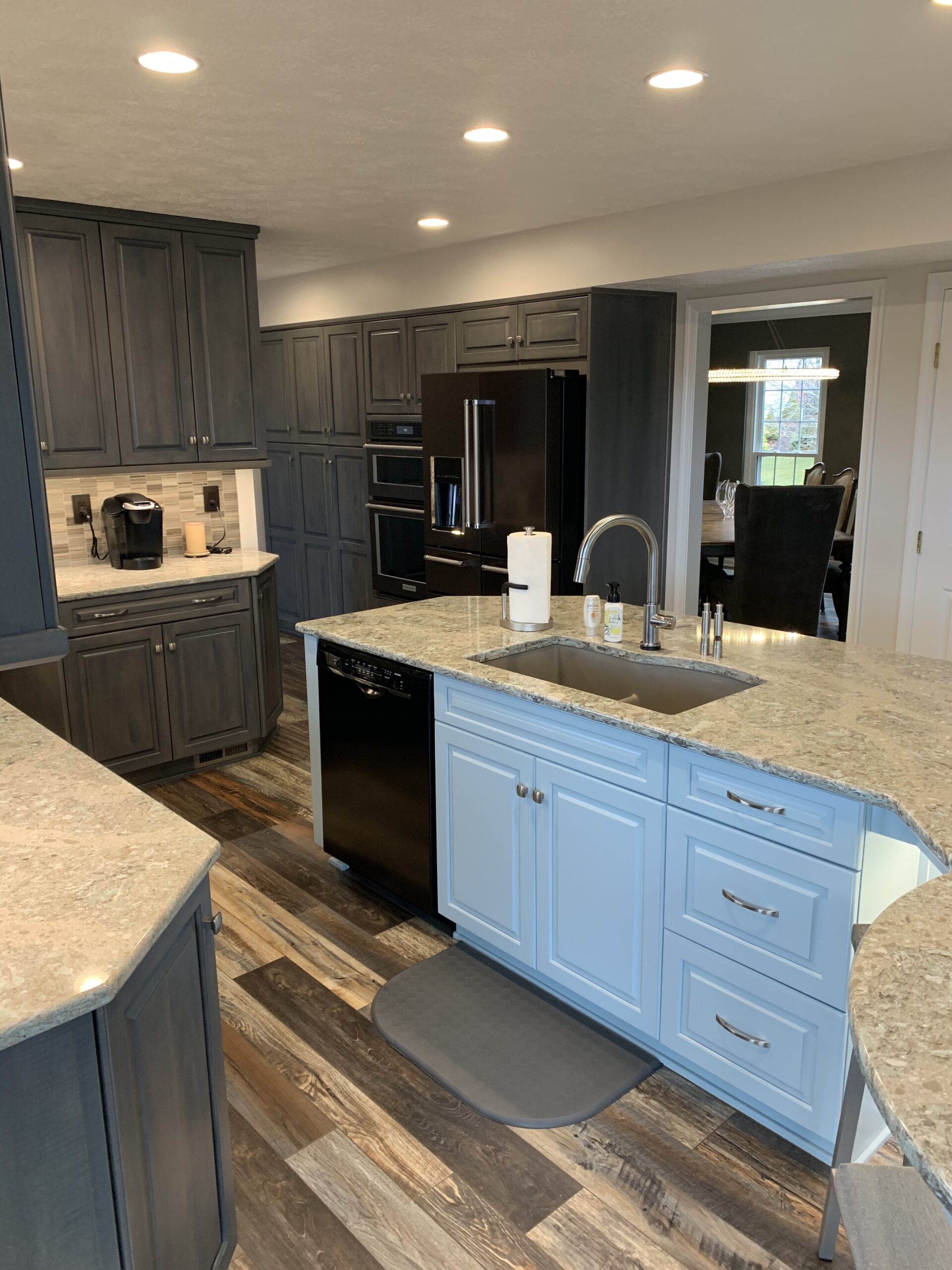 Classic kitchen, grey marble island and lighting, dark cabinets, marble counter, brown-shade floor, modern tile backsplash