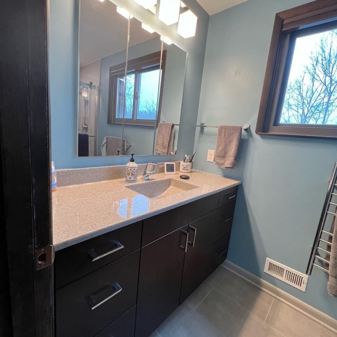 Classic bathroom remodel, light blue walls, light color marble countertop sink, dark cabinet storage, window