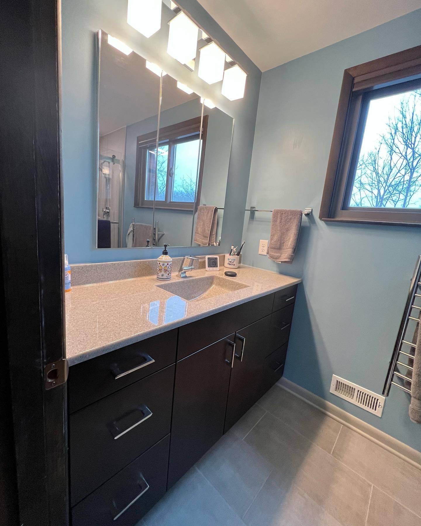 Classic bathroom remodel, light blue walls, light color marble countertop sink, dark cabinet storage, window