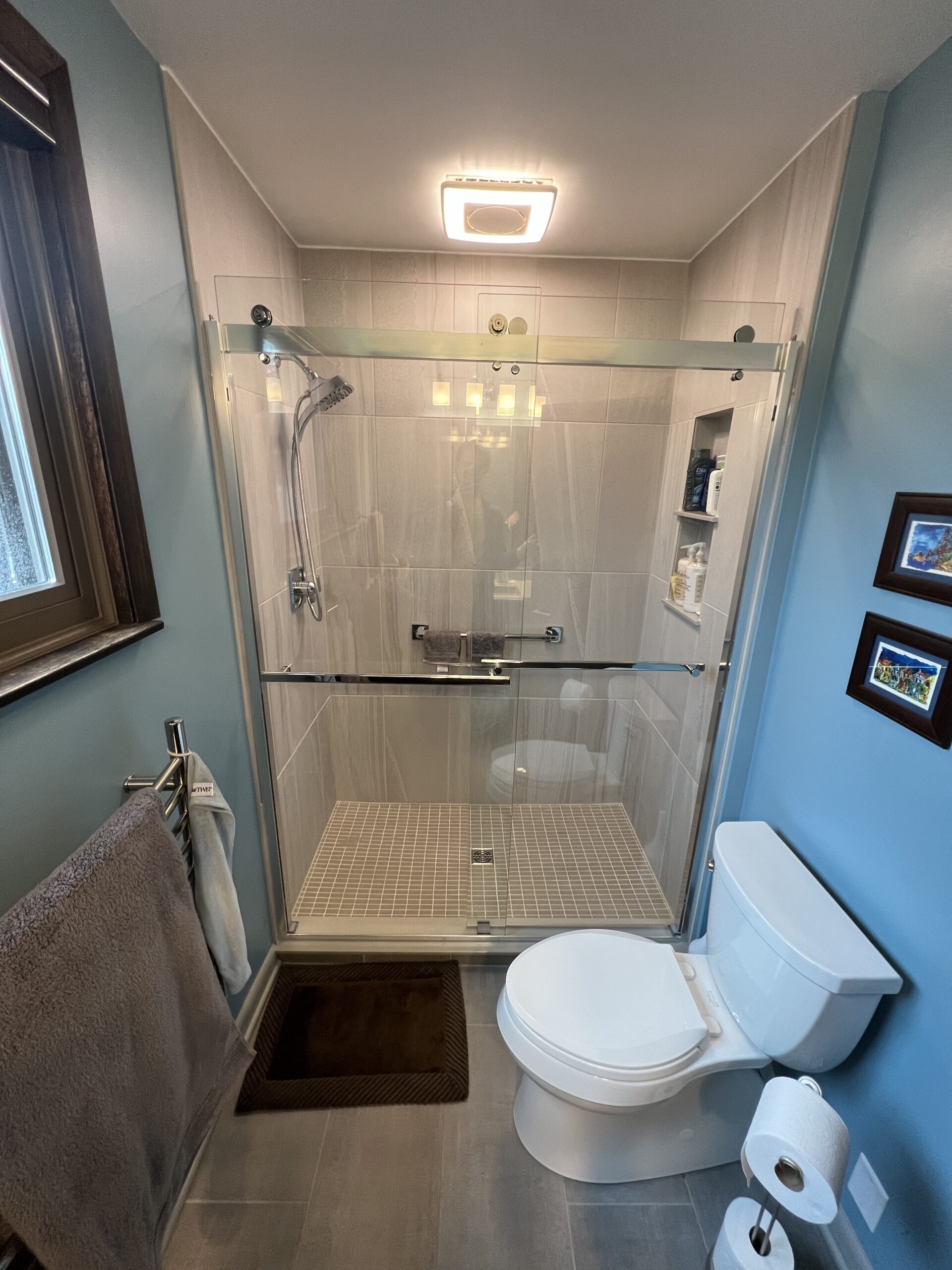 Classic blue bathroom remodeling, light gray shower tile walls, small beige square tile floor, two piece toilet toilet