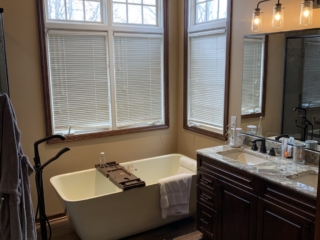 Classic bathroom, white soaking tub, double sink with dark cabinet storage, brown floor, windows