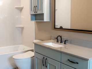 Classic small bathroom, sink with blue cabinet storage, shower/bath tub with small shelves, original floor tiles, one-piece toilet