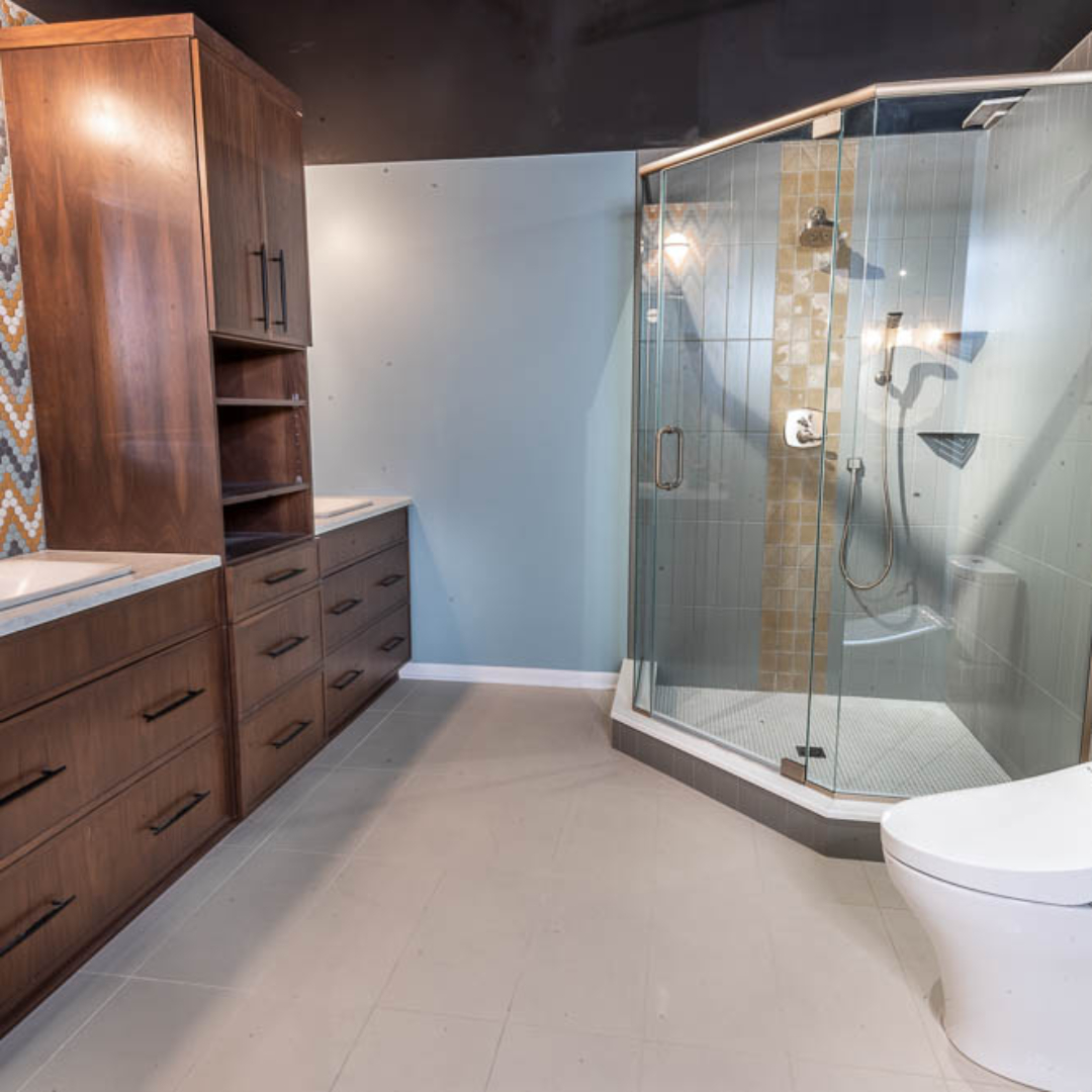 Traditional bathroom, two single sink with white marble countertop and brown wooden cabinets separated by a closet, large shower, one-piece toilet