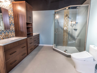 Traditional bathroom, two single sink with white marble countertop and brown wooden cabinets separated by a closet, large shower, one-piece toilet