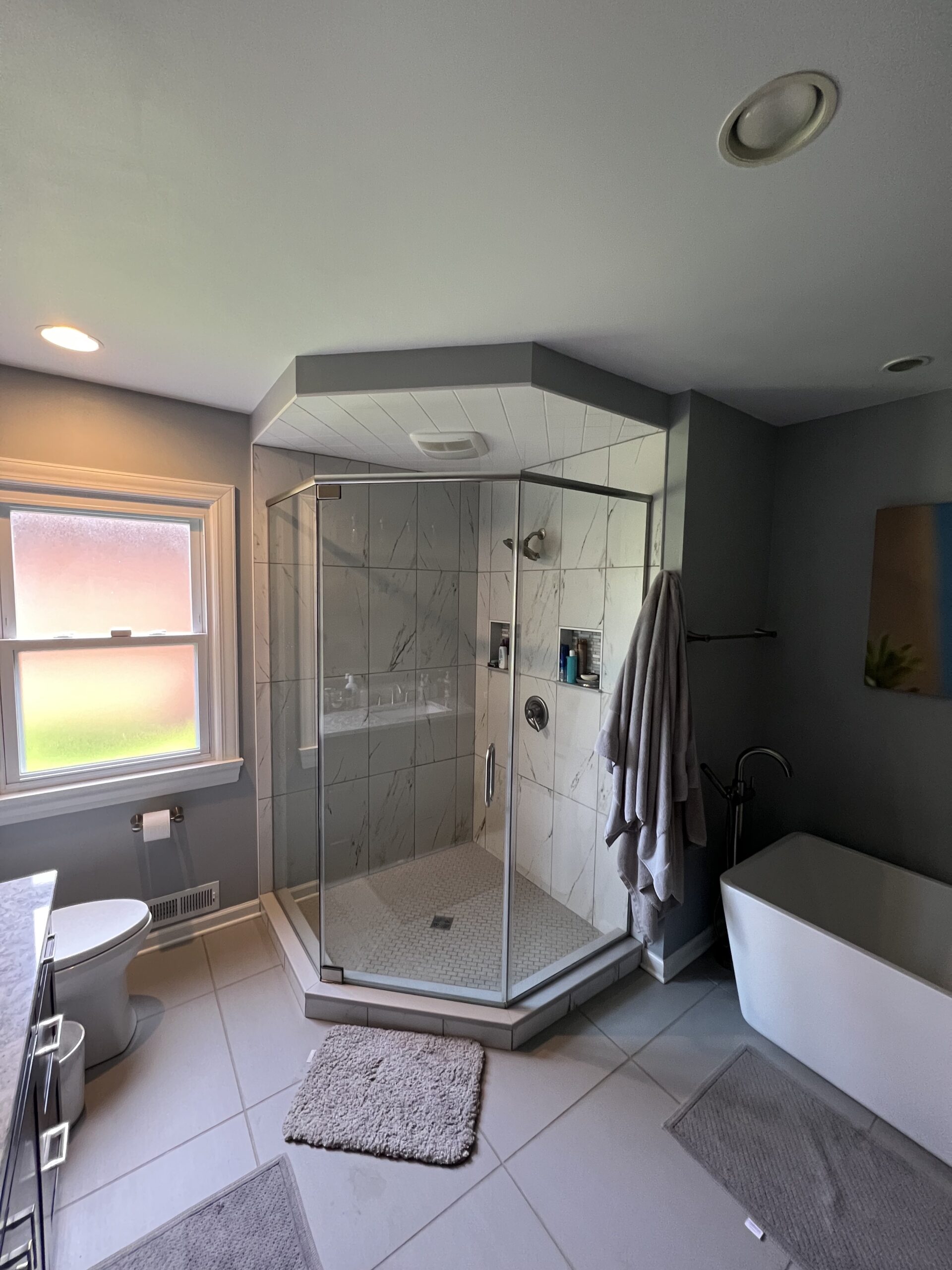 Contemporary bathroom, big shower with large light colored marble tiles, white soaking tub, blurry window