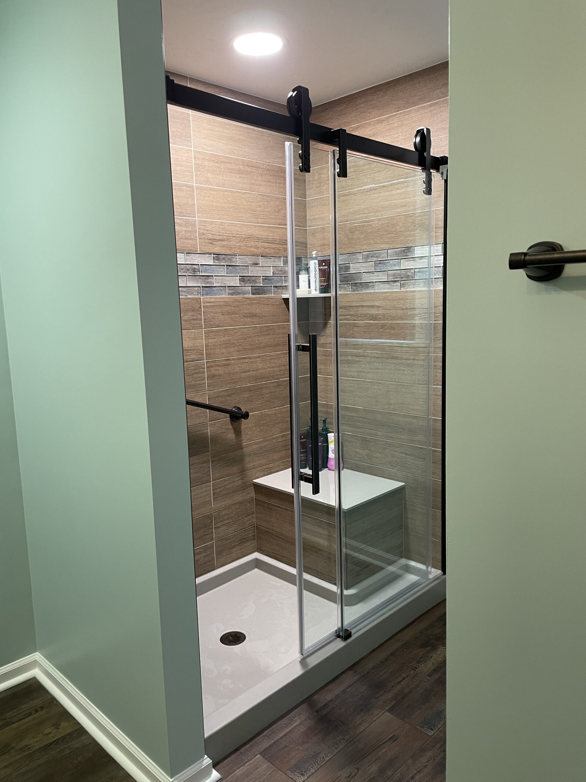 Contemporary green bathroom, brown shower tiles, black shower frame, grey marble shower strap