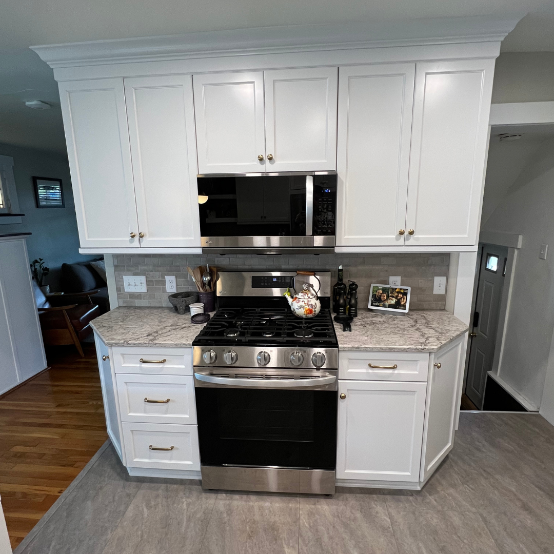 Classic kitchen remodel with small marble counter, white cabinets and storage, black stove and microwave