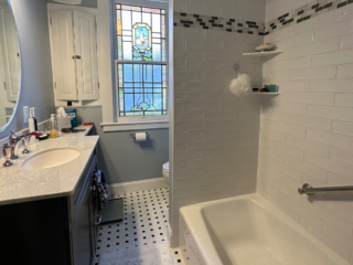 Traditional small bathroom remodel with classic bathtub/shower, single sink with black cabinet storage, black and white floor tiles, window
