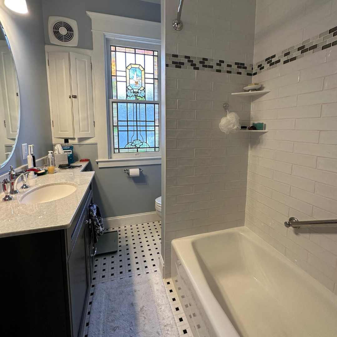 Traditional small bathroom remodel with classic bathtub/shower, single sink with black cabinet storage, black and white floor tiles, window