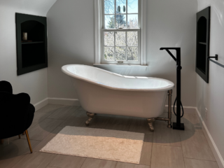 White vintage bathtub with small black shower and modern floor tiles, window
