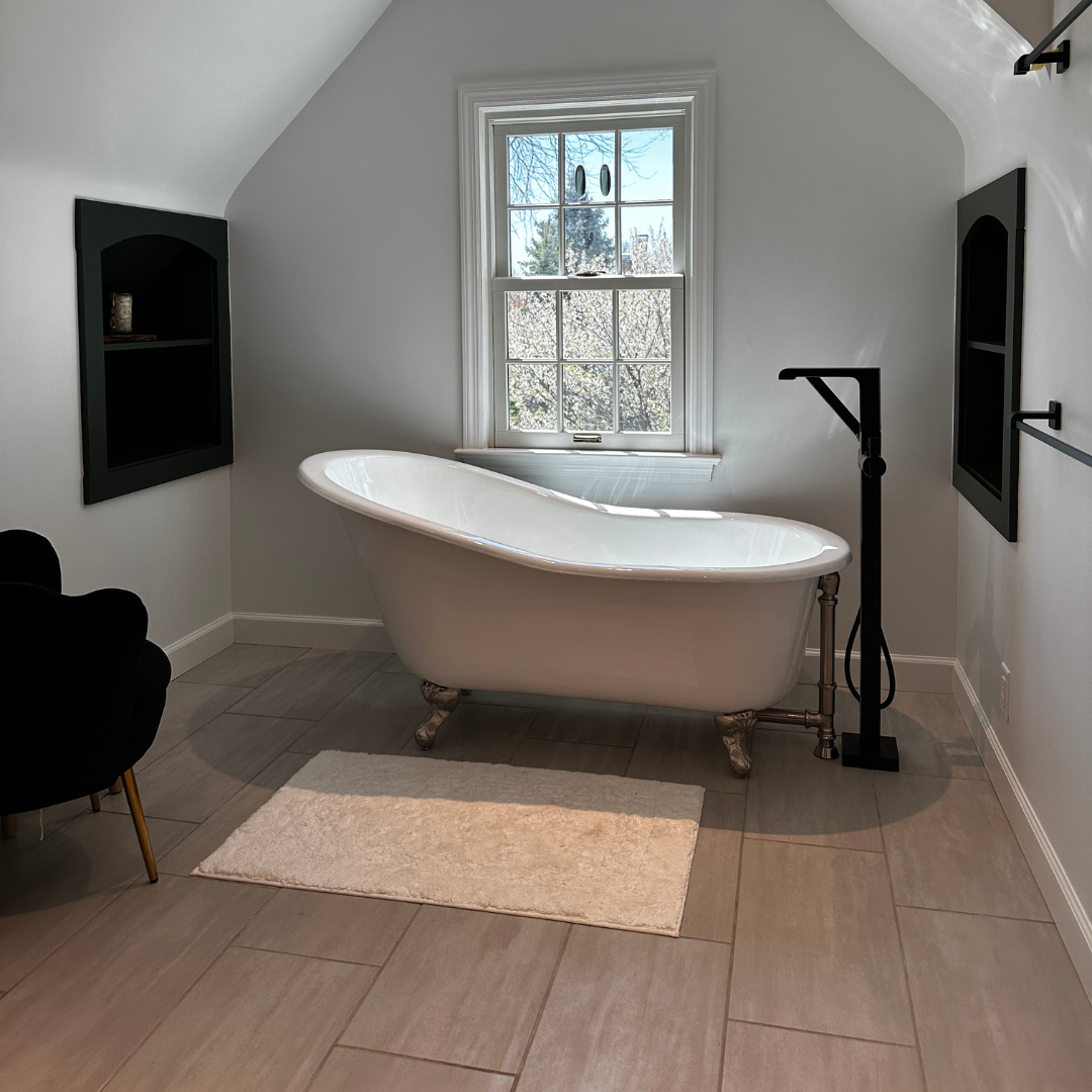 White vintage bathtub with small black shower and modern floor tiles, window