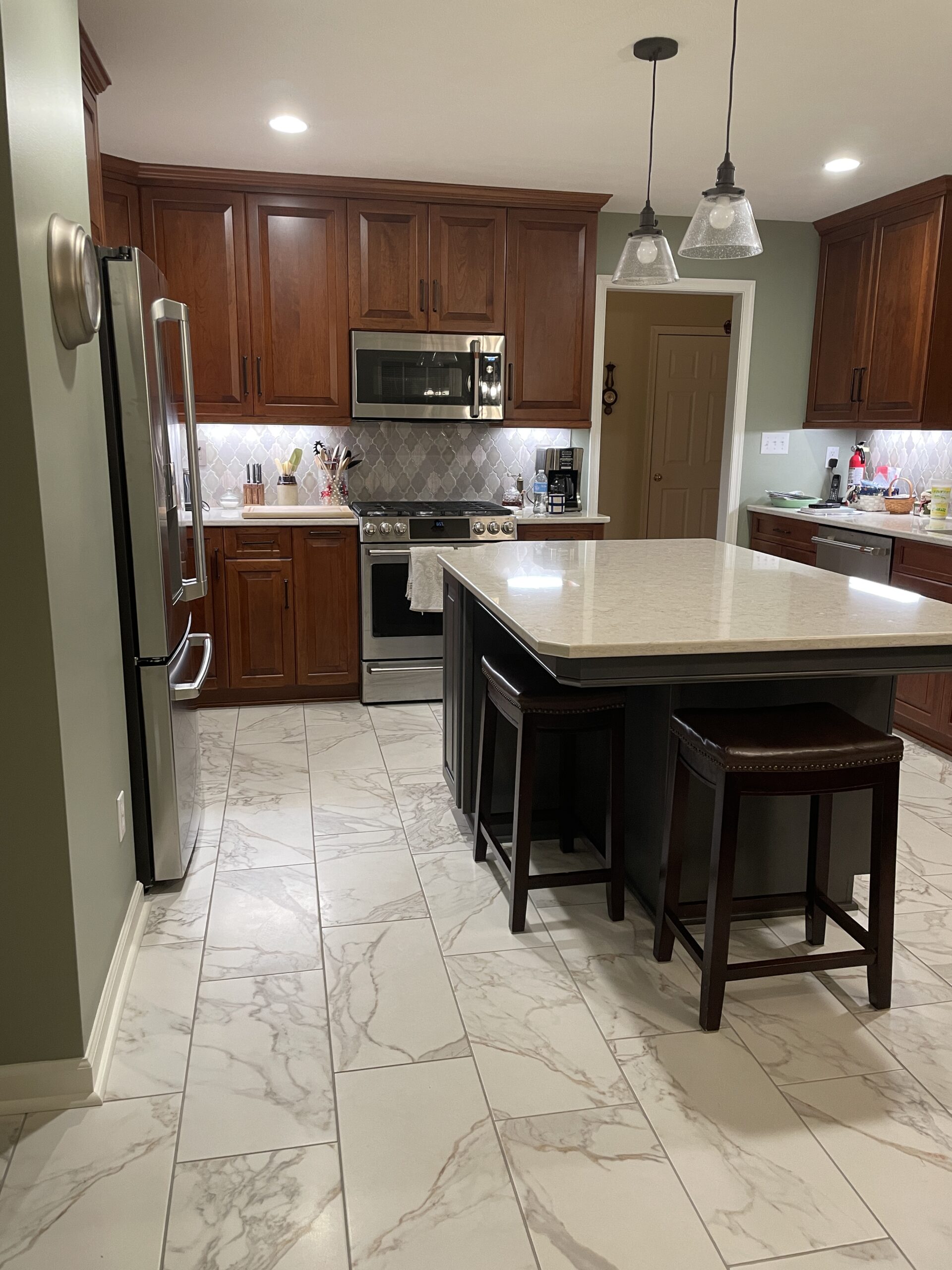 Classic kitchen, center table with white marble countertop, brown cabinets and storage, arabesque tile backsplash, black and white floor tiles