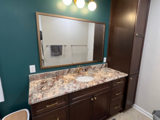 Modern bathroom sink, brown cabinets and drawers, mixed brown colored countertop with single sink, big mirror and modern lights