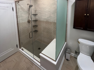 Modern bathroom shower, white wall tiles on top and brown ones downwards, shelves, grey hexagonal floor shower tiles