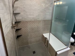 Modern bathroom shower, white wall tiles on top and brown ones downwards, shelves, grey hexagonal floor shower tiles