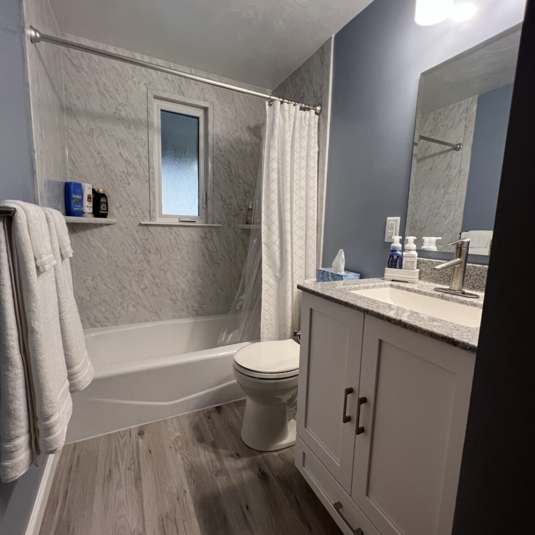 Classic small bathroom, shower and bathtub, blue walls, black and white marble shower walls, two-piece toilet