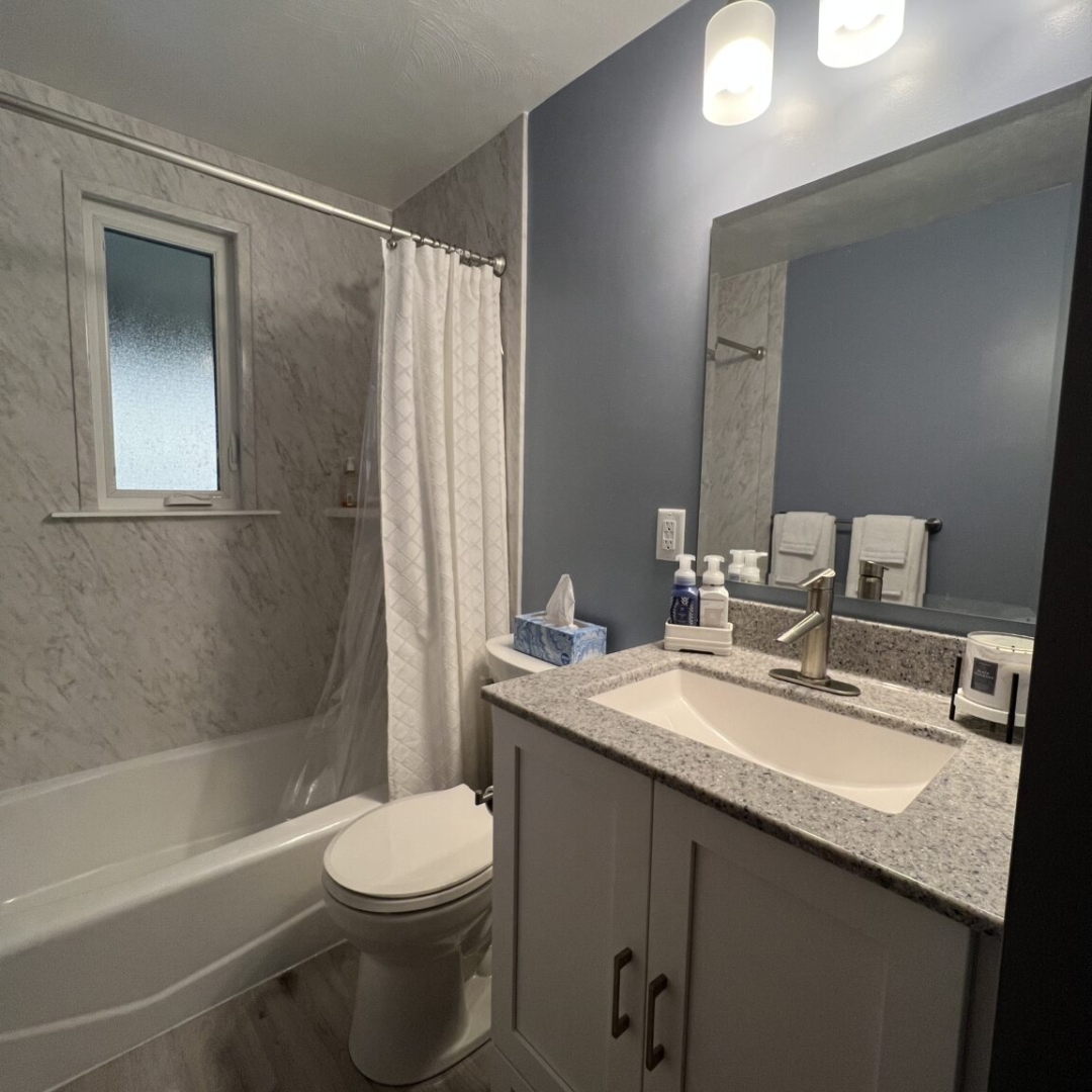 Classic small bathroom, shower and bathtub, blue wall, crushed marble sink with white cabinet, two-piece toilet