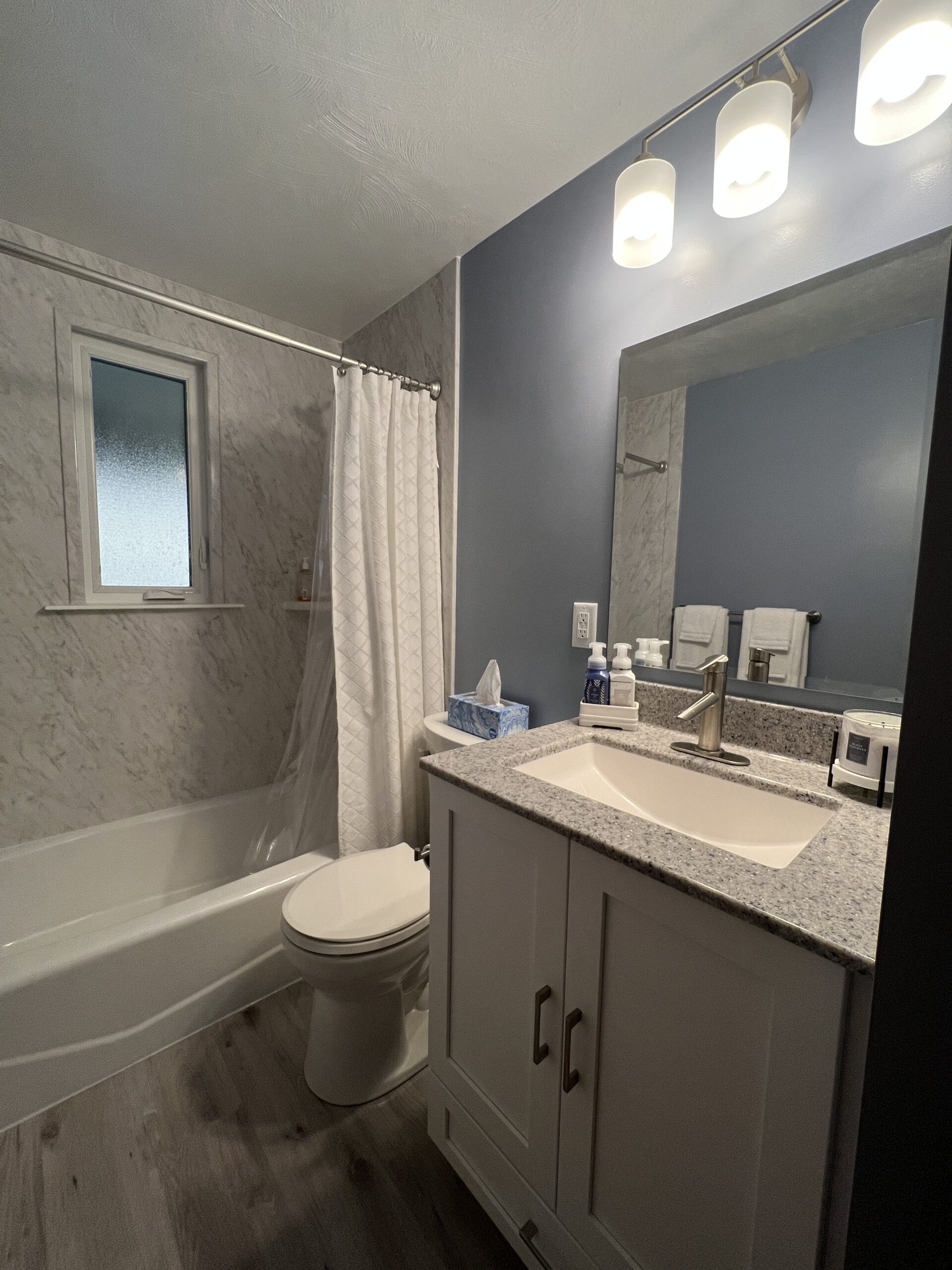 Classic small bathroom, shower and bathtub, blue wall, crushed marble sink with white cabinet, two-piece toilet