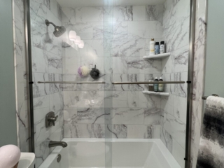 Modern bathroom, black and white marble walls, small shelves, shower head, bathtub