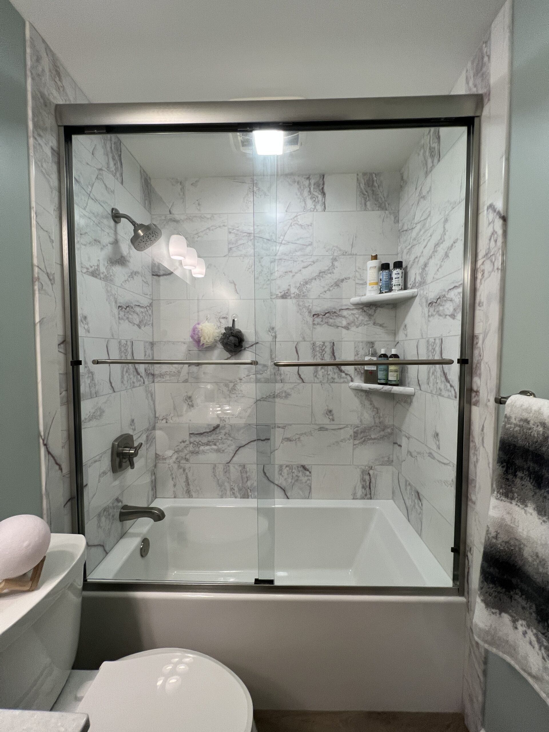 Modern bathroom, black and white marble walls, small shelves, shower head, bathtub