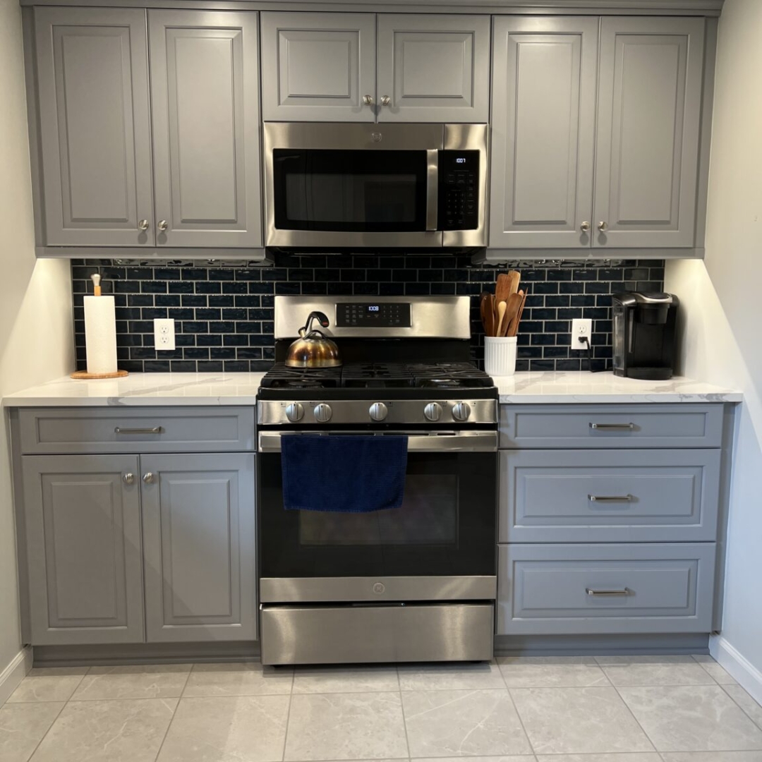 Grey kitchen cabinets, navy subway tile backsplash, stainless steel stove and microwave, white marble countertops, elegant design