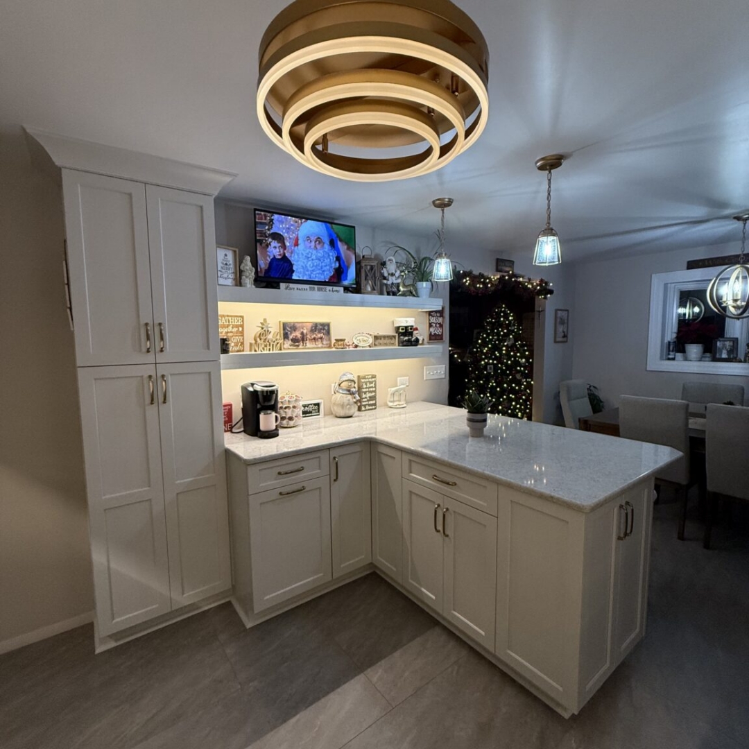 Kitchen remodel with white shaker cabinetry, quartz countertops, white subway tile backsplash, brass and gold hardware, retractable ceiling fan light fixture, glass pendant lights, white and gold bar stools, floating shelves with underlighting, and stainless steel appliances