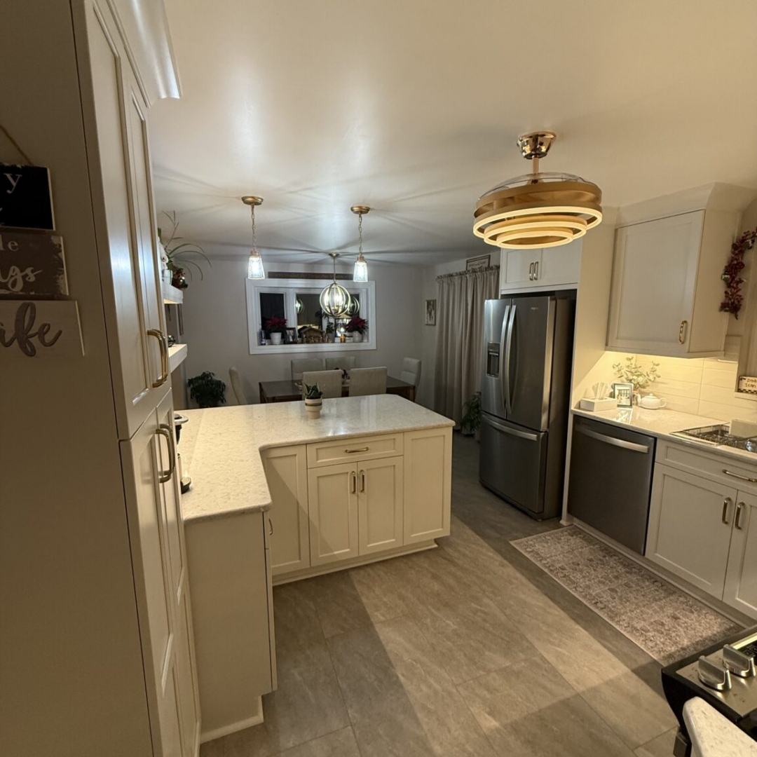 Kitchen remodel with white shaker cabinetry, quartz countertops, white subway tile backsplash, brass and gold hardware, retractable ceiling fan light fixture, glass pendant lights, white and gold bar stools, floating shelves with underlighting, and stainless steel appliances