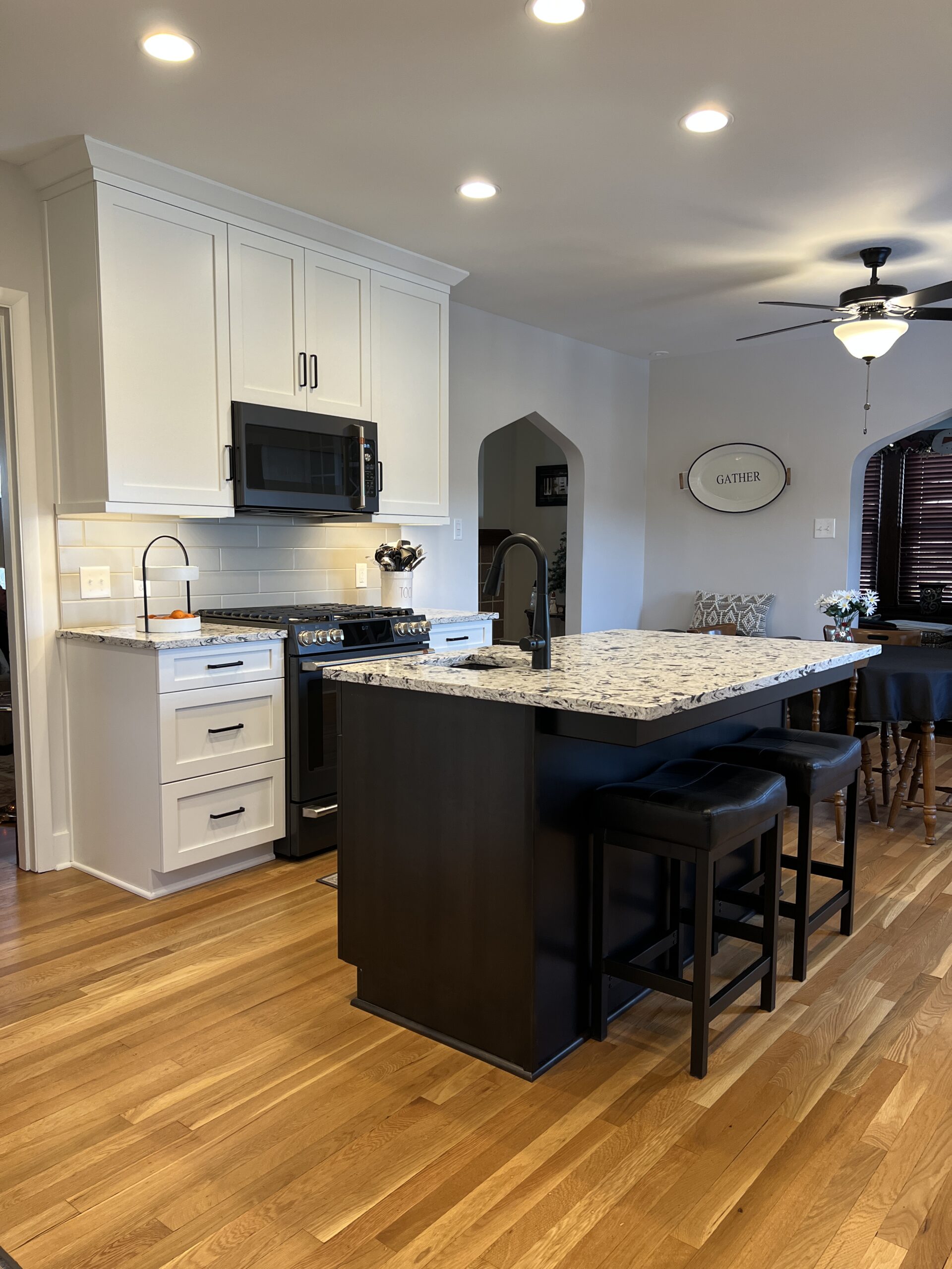 Modern black and white kitchen, black island with black and white marble countertop, white wall and base cabinets, light brown floors, butlers pantry