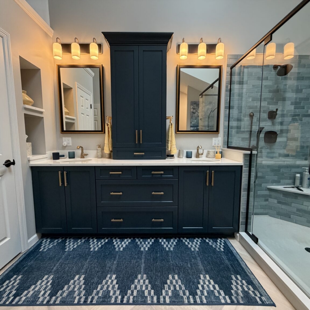 Luxury bathroom remodel featuring navy blue double vanity with brass hardware, quartz countertop, blue-grey subway tile walk-in shower, freestanding soaking tub with floor-mount tub filler, herringbone tile floor, and skylights