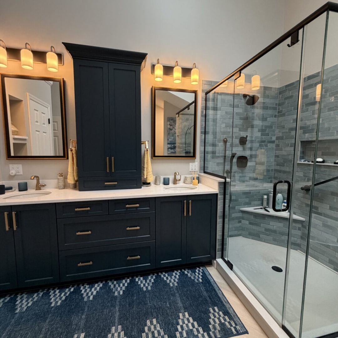 Luxury bathroom remodel featuring navy blue double vanity with brass hardware, quartz countertop, blue-grey subway tile walk-in shower, freestanding soaking tub with floor-mount tub filler, herringbone tile floor, and skylights