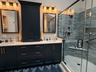 Luxury bathroom remodel featuring navy blue double vanity with brass hardware, quartz countertop, blue-grey subway tile walk-in shower, freestanding soaking tub with floor-mount tub filler, herringbone tile floor, and skylights