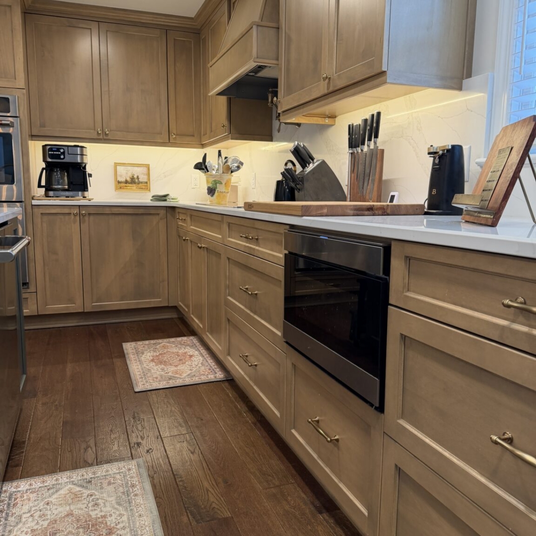 Kitchen remodel with warm taupe stained cabinetry, contrasting slate blue island with brass hardware, quartz countertops, marble-look tile backsplash, custom range hood, hardwood floors, pendant lighting, and stainless steel appliances