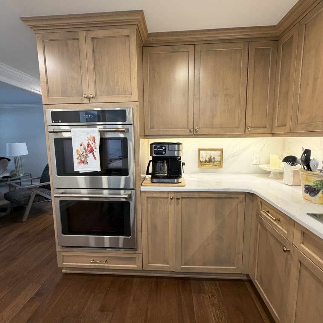 Kitchen remodel with warm taupe stained cabinetry, contrasting slate blue island with brass hardware, quartz countertops, marble-look tile backsplash, custom range hood, hardwood floors, pendant lighting, and stainless steel appliances