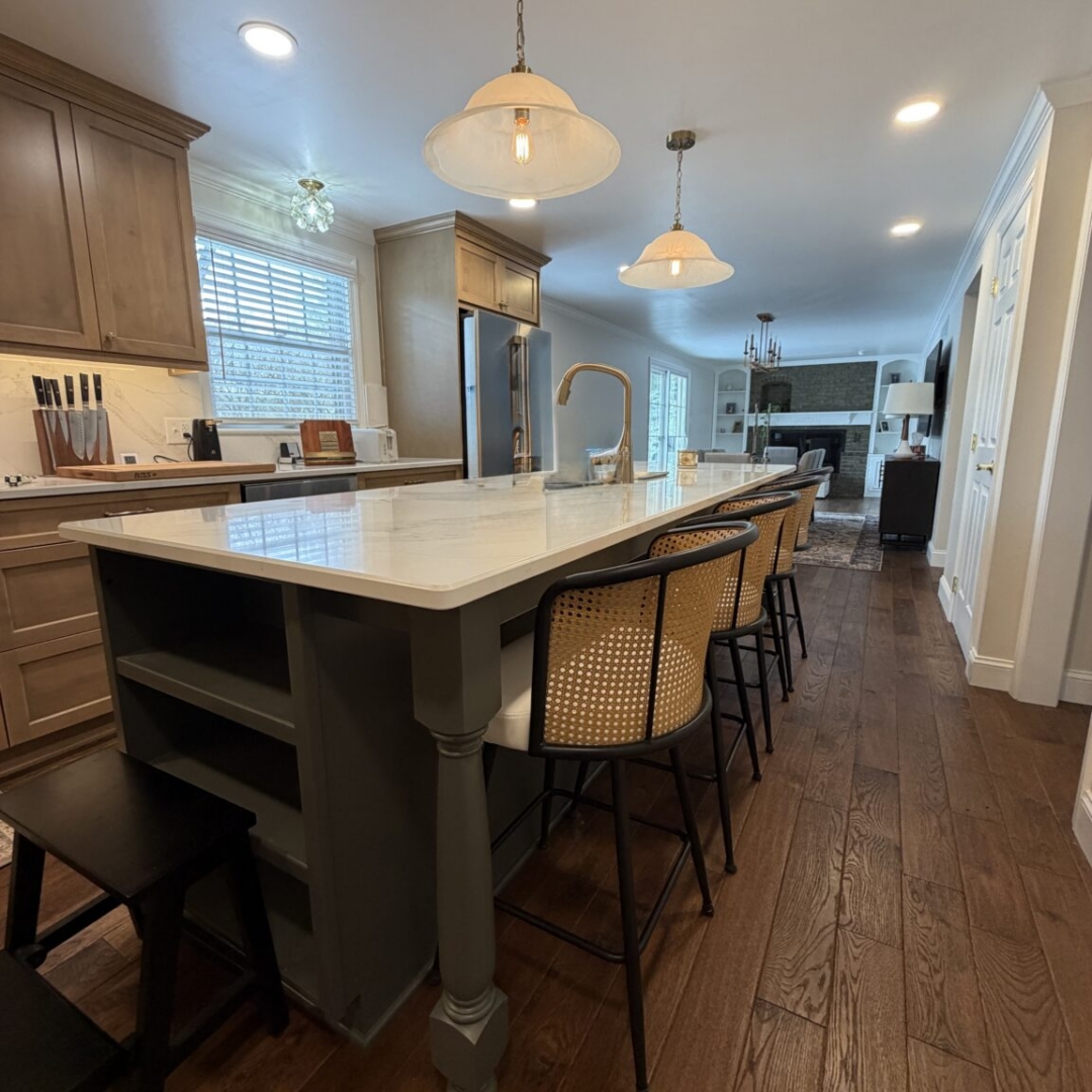 Kitchen remodel with warm taupe stained cabinetry, contrasting slate blue island with brass hardware, quartz countertops, marble-look tile backsplash, custom range hood, hardwood floors, pendant lighting, and stainless steel appliances