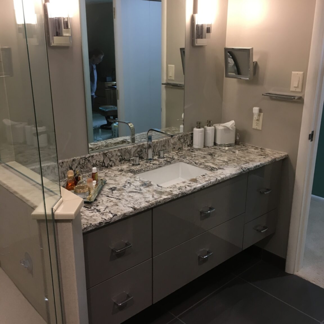 Granite countertop, grey bathroom cabinets, large mirror with vanity lighting, dark floor tiles, storage drawers, elegant