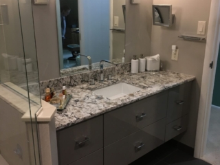Granite countertop, grey bathroom cabinets, large mirror with vanity lighting, dark floor tiles, storage drawers, elegant