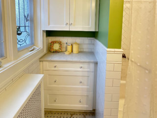 Traditional bathroom, white wall and base cabinets and drawers with marble countertop, light green walls, windows, original white and grey floor tiles