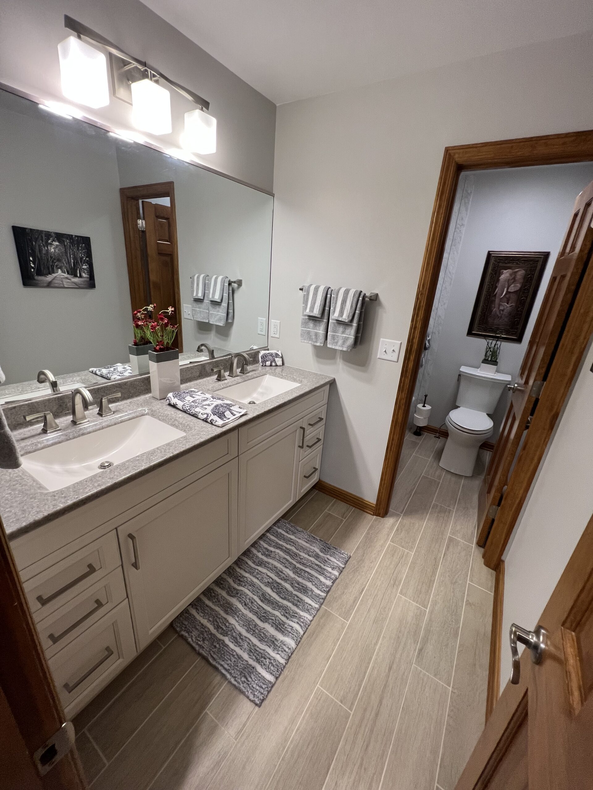 Classic bathroom, double sink, grey marble countertop, white cabinets, large mirror, modern brown floor tiles