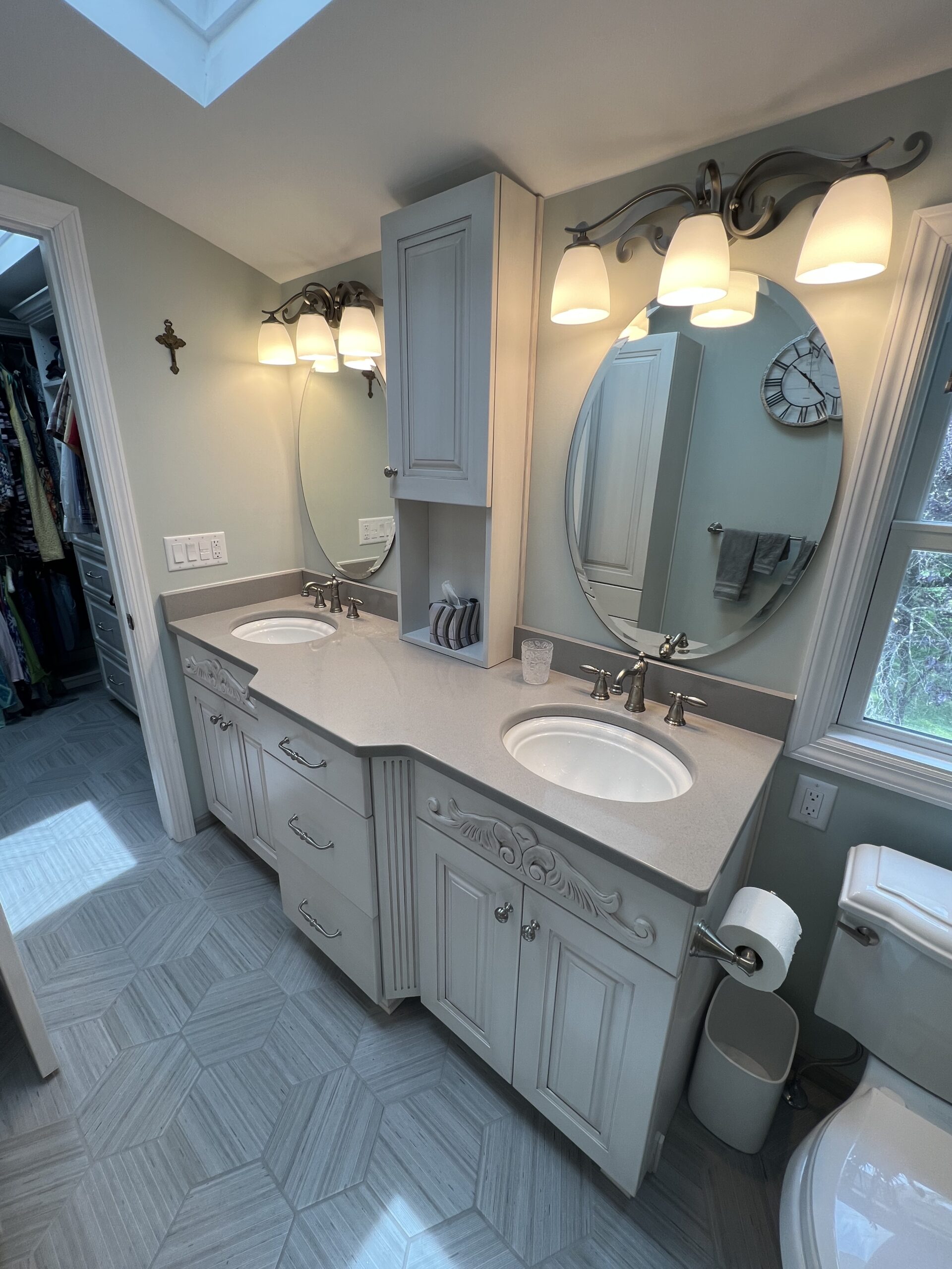 Traditional bathroom, vintage double sink, grey marble countertop, two round-shaped mirrors, window, toilet