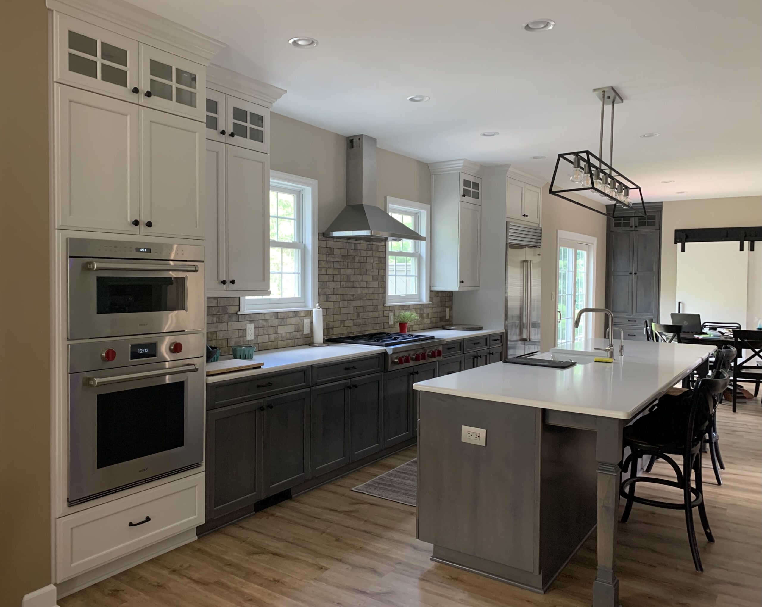 Modern kitchen remodel, island with grey cabinets and white countertop, white wall cabinets, dark grey base cabinets, subway tile backsplash, traditional cooker hood